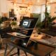 Coin de coworking cosy et éclectique avec bureau debout, fauteuils confortables, suspensions lumineuses et abondance de plantes en pot.