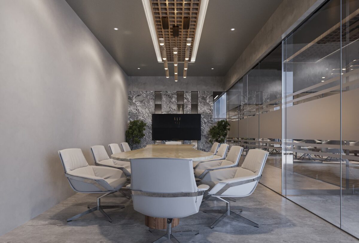 Une salle de réunion moderne avec une grande table ovale en pierre, des chaises confortables blanches, des murs en béton et une grande télévision murale. Les parois vitrées donnent sur d'autres espaces de travail.