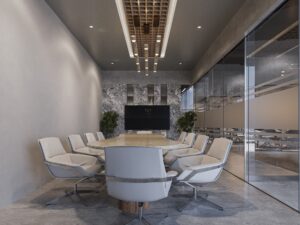 Une salle de réunion moderne avec une grande table ovale en pierre, des chaises confortables blanches, des murs en béton et une grande télévision murale. Les parois vitrées donnent sur d'autres espaces de travail.